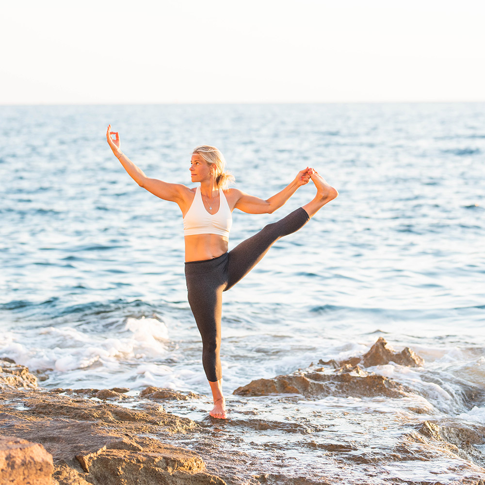 Charlotte F som står på en sten i vattnet och gör yogapose.