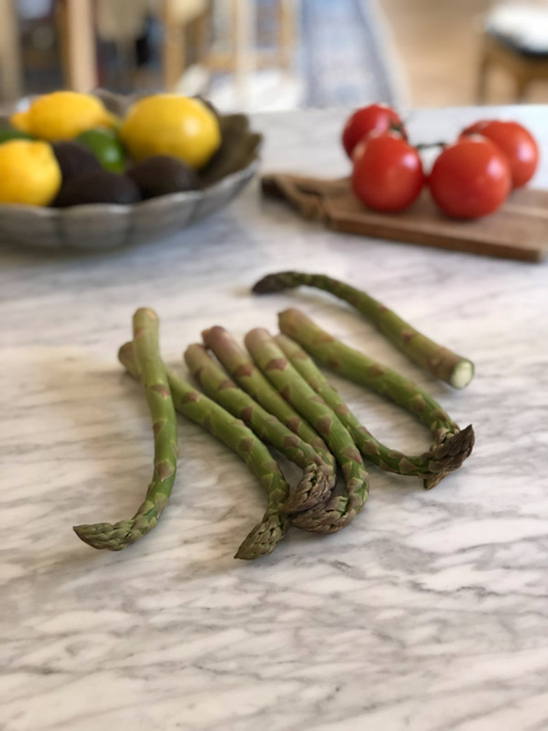 Sparris som ligger på en köksbänk med tomater och citron