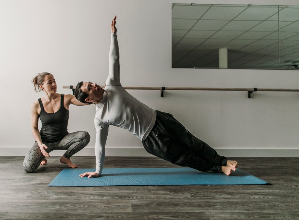 En kvinna instruerar en man gällande en yogaposition.